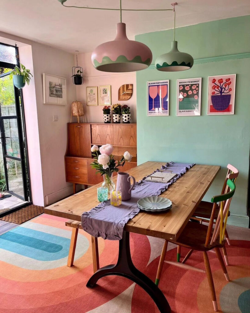 Picture of a dining room with green and pink walls, a wooden dining table with chairs, and multi-colored accessories.