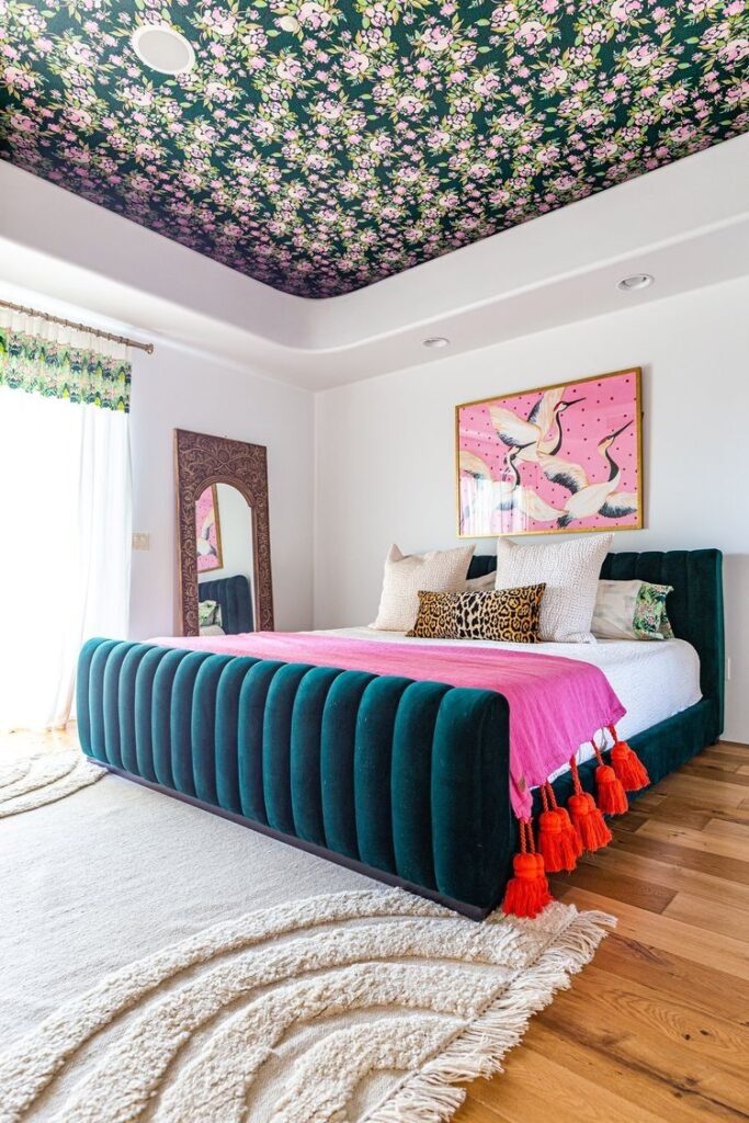 Picture of a bedroom with white walls and green and pink floral ceiling wallpaper. 