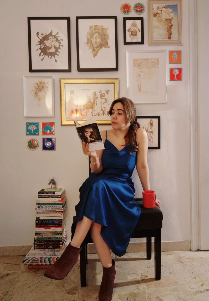 Girl sitting in front of a picture wall, holding a book, reading for a book review.