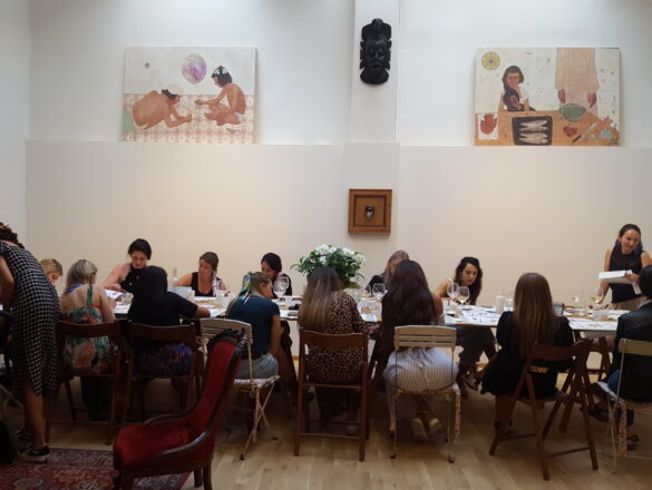 A long table inside an art gallery with girls sitting and painting with wine.