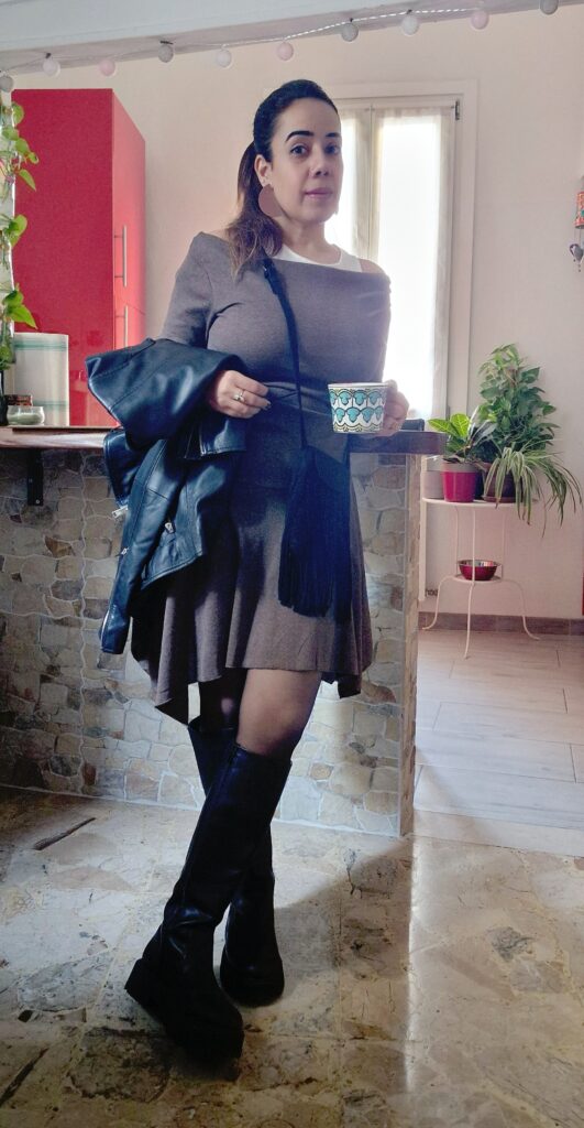 Picture of the author standing in front of her kitchen countertop holding a coffee cup and a black leather jacket. 